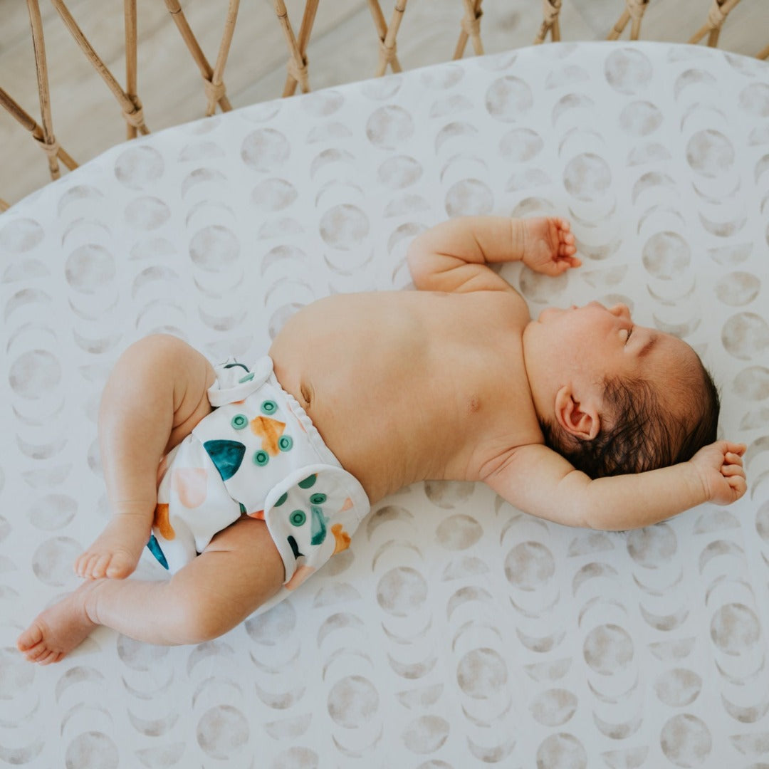 Newborn baby laying on their back in a bassinet stretching wearing a reusable cloth nappy.