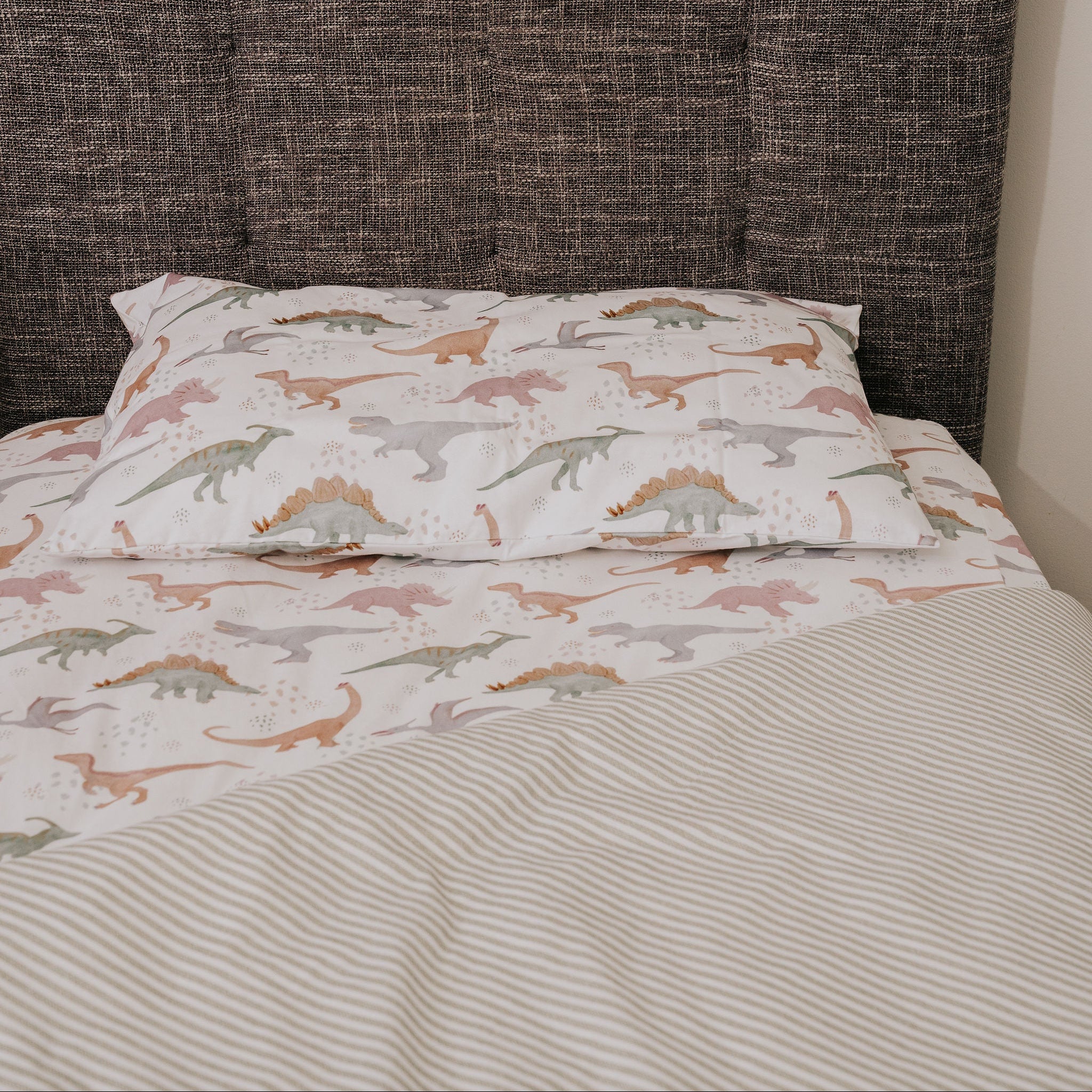 Bed with dinosaur-patterned bedding and a textured headboard.