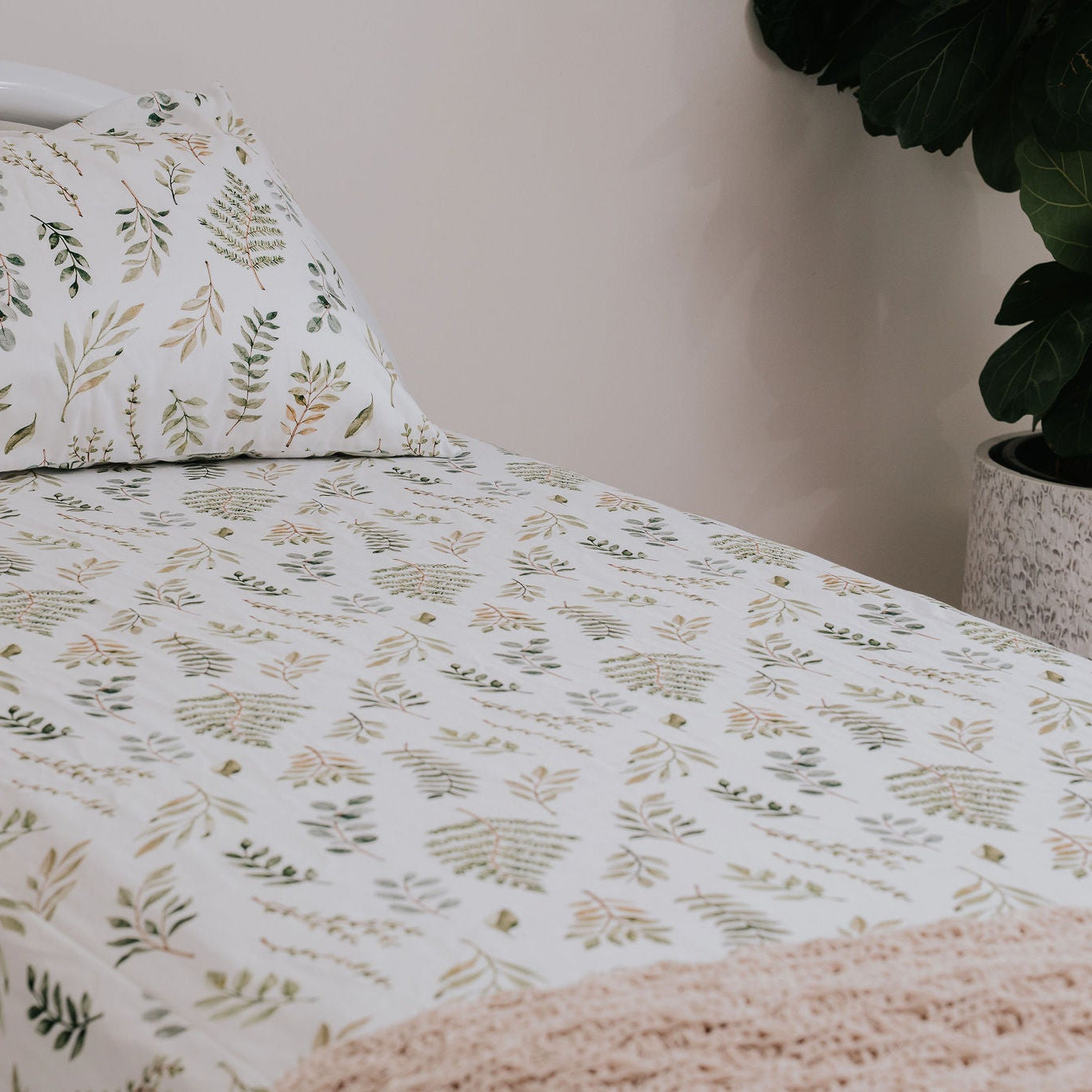 Leaf-patterned bedspread on a bed with a plant in the corner