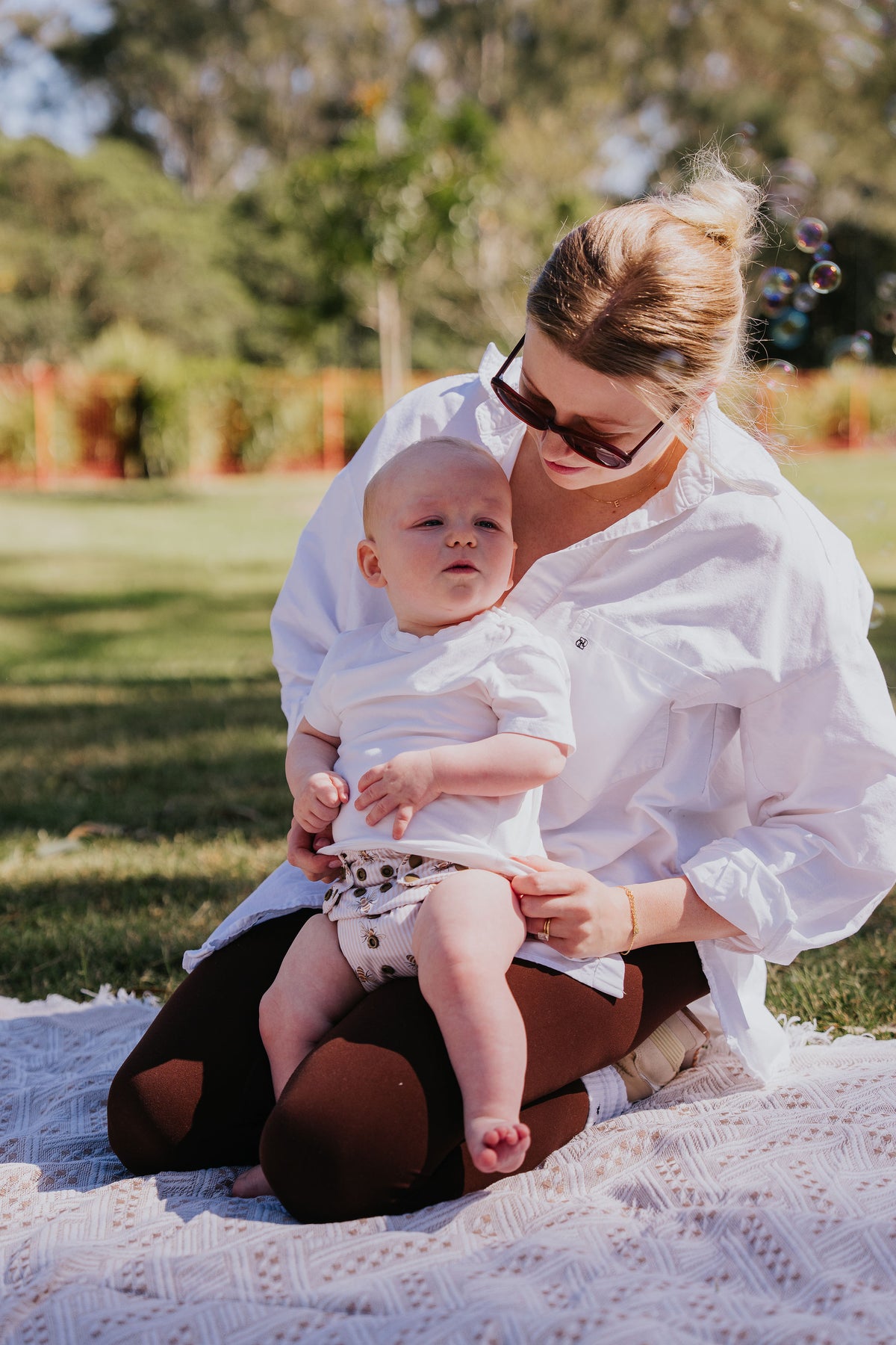 Baby sitting on mum's lap at a picnic wearing a Pixie cloth nappy in Beeline print