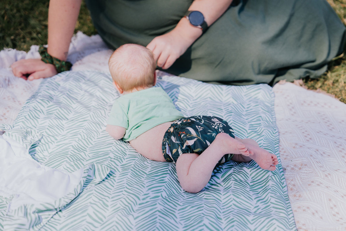 Baby doing tummy time on a picnic rug wearing a Pixie cloth nappy in Evergreen print