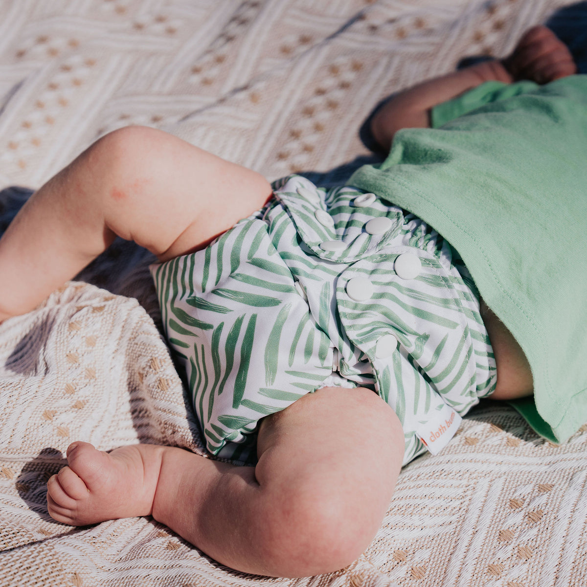 Close-up of a baby lying on a blanket wearing a Pixie cloth nappy in Greenhouse print