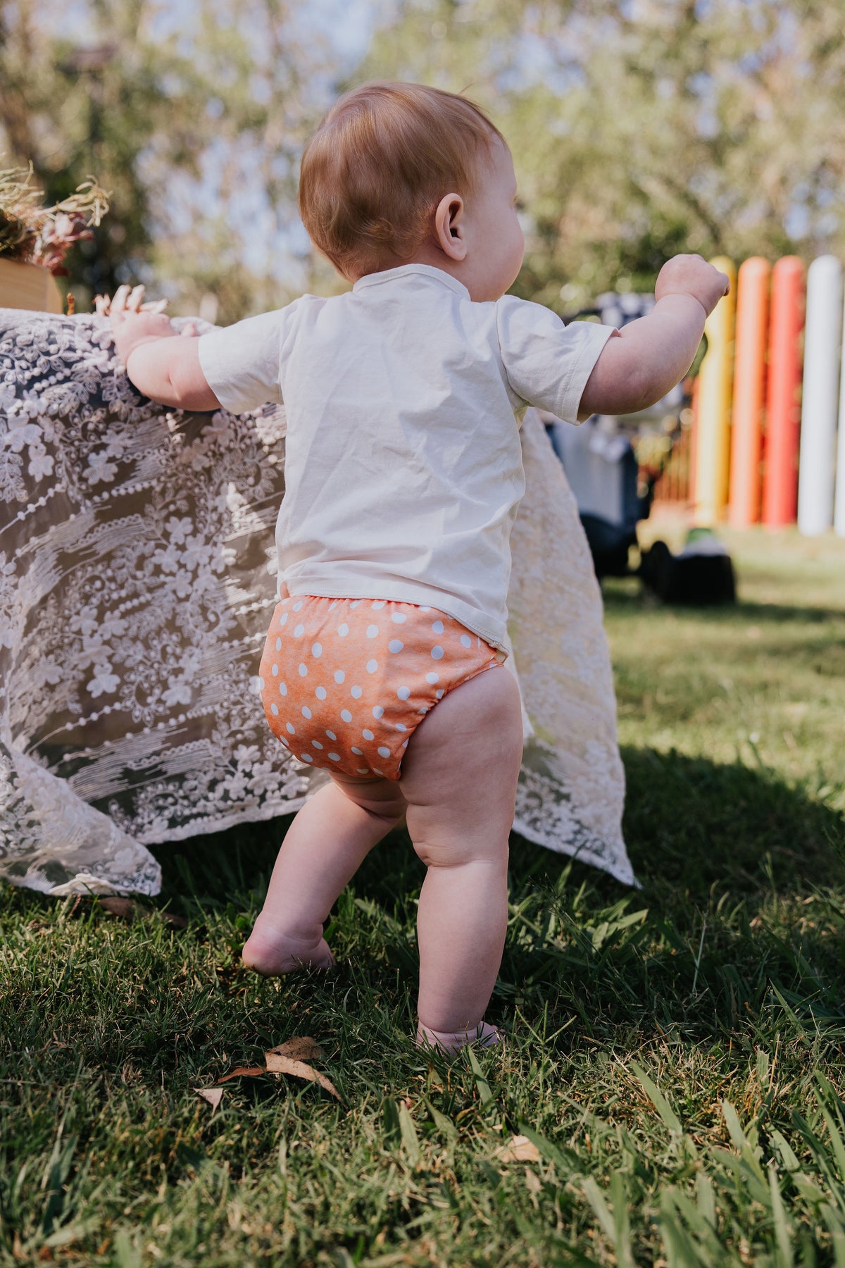 Baby holding onto a table on the grass wearing a Pixie cloth nappy in Marmalade print