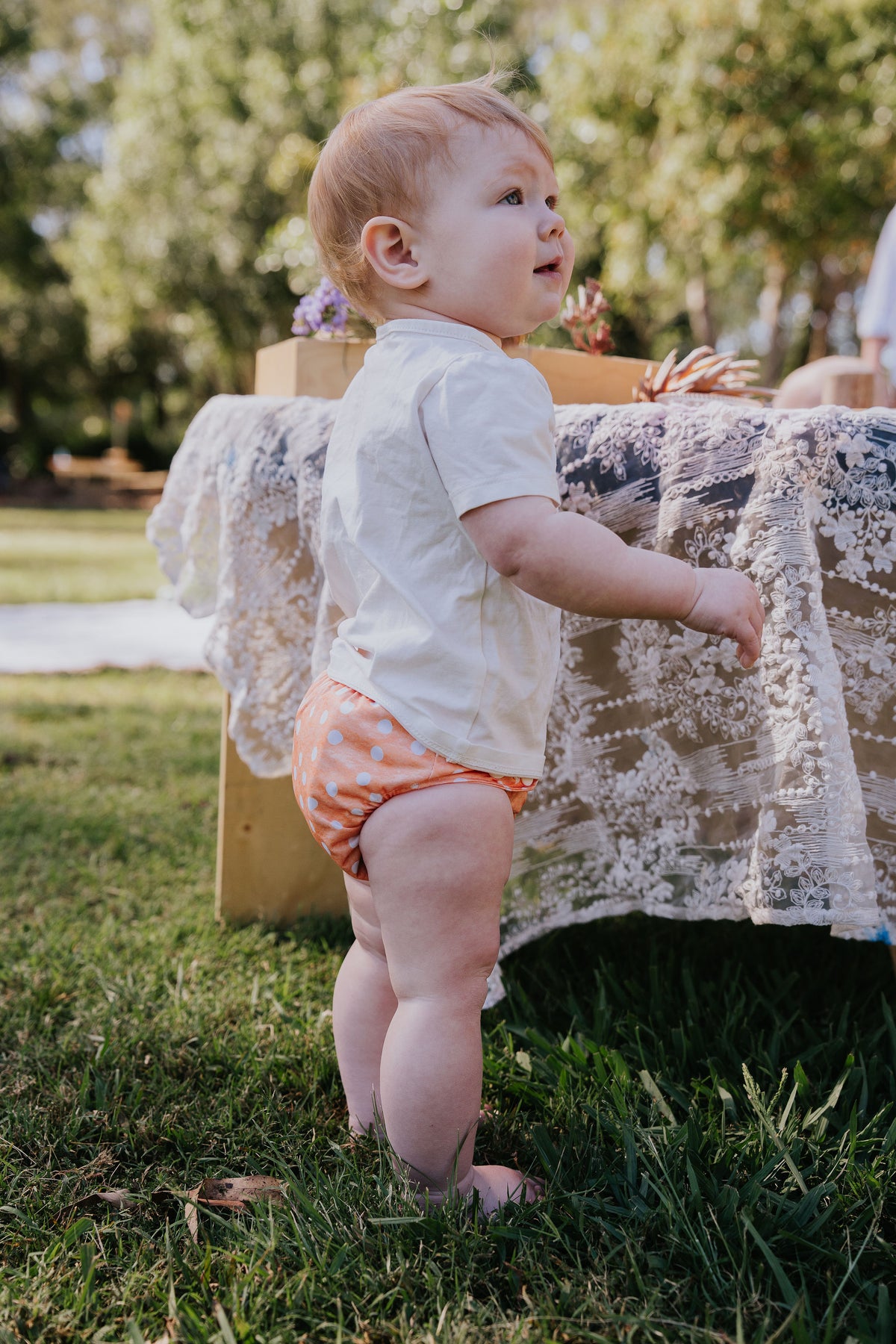 Baby standing on the grass wearing a Pixie cloth nappy in Marmalade print