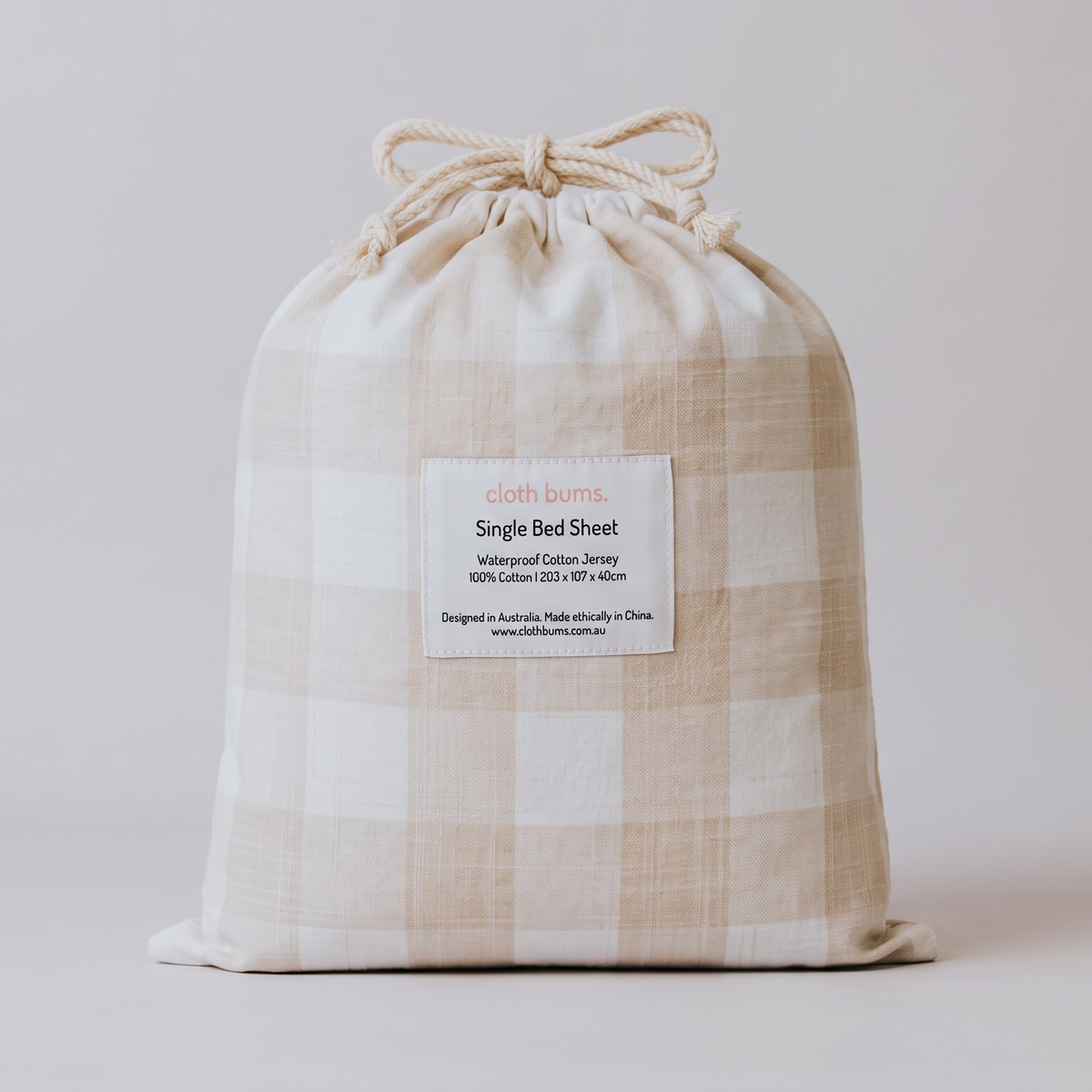 A single bed sheet in a beige and white gingham check pattern, neatly folded and packed inside a matching fabric drawstring bag with a white label in the center.