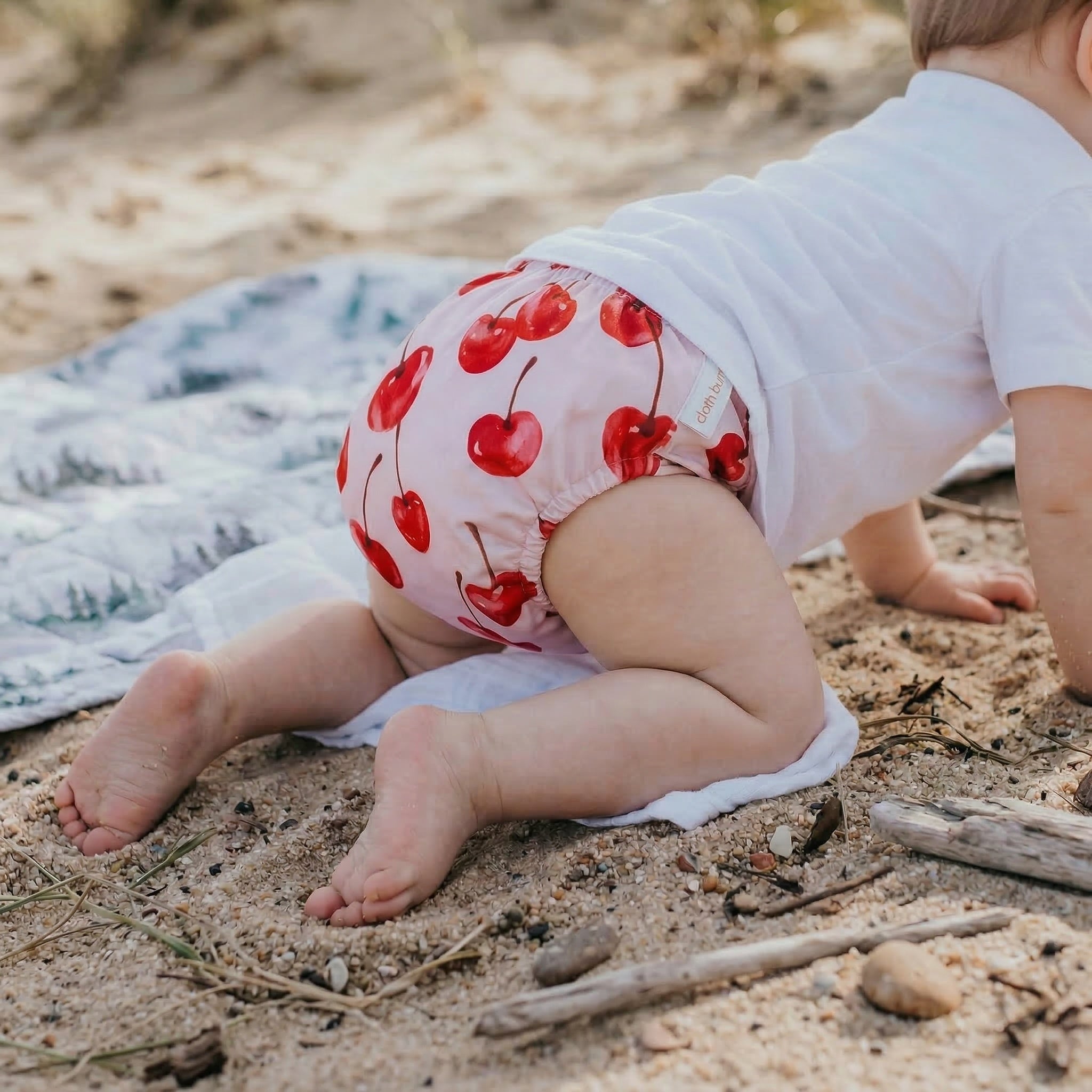 Baby in a diaper with red cherry pattern on a sandy surface