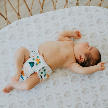 Newborn baby laying on their back in a bassinet stretching wearing a reusable cloth nappy. 