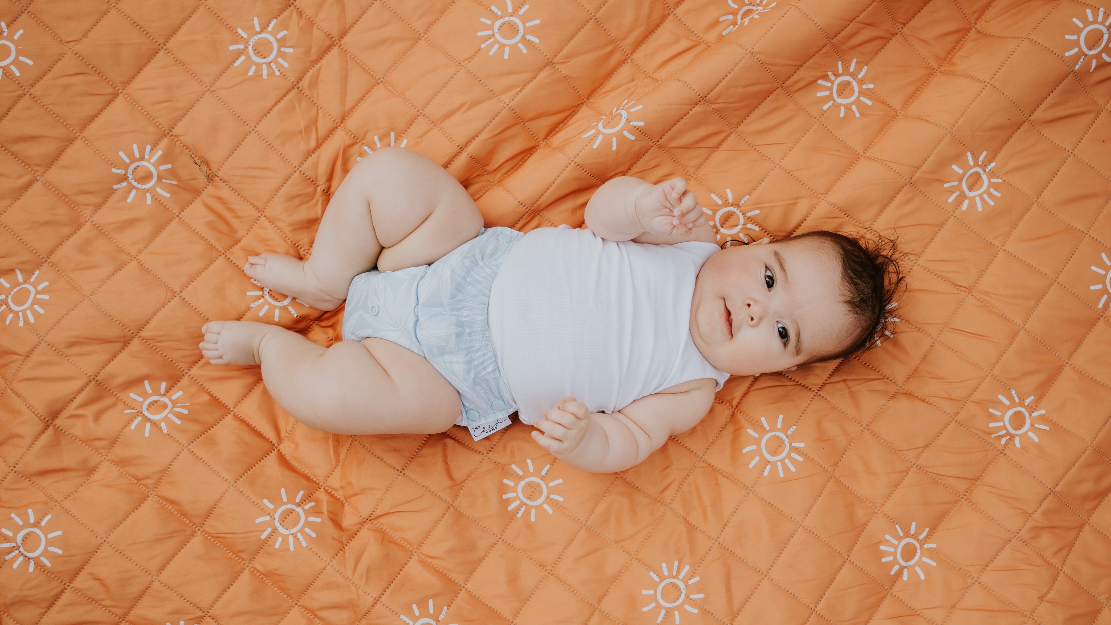 Baby lying on an orange quilt with sun patterns