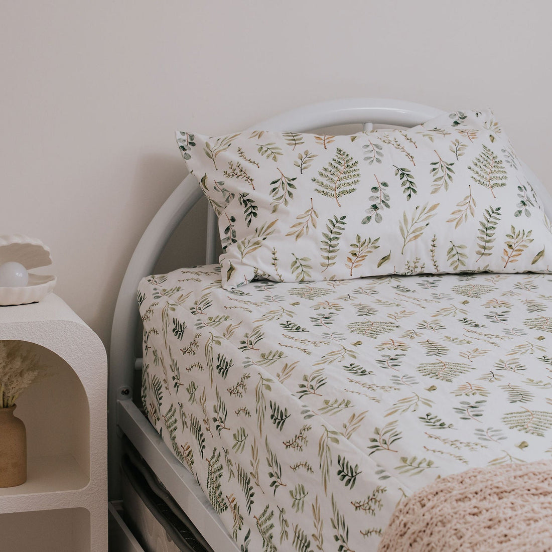 Bed with leafy bedding next to a nightstand with decorative items.