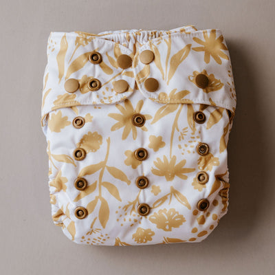 A cloth diaper with a golden floral pattern and snap closures.