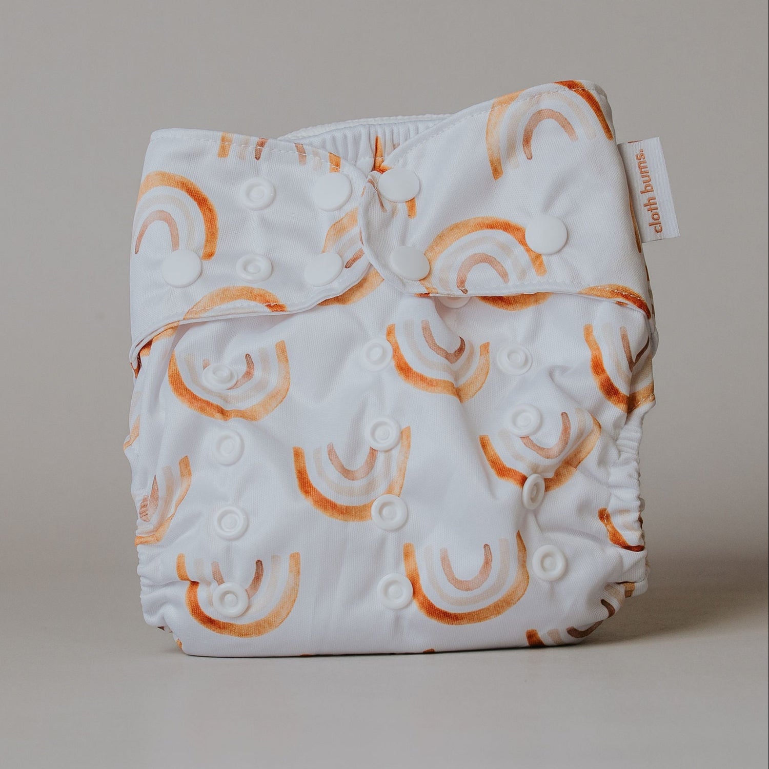 White cloth diaper with orange rainbow patterns on a beige background