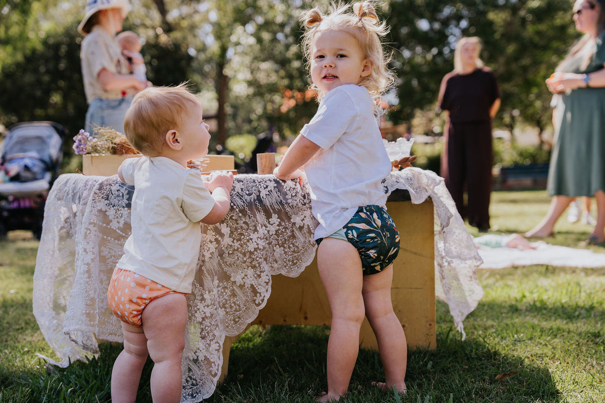 Two toddlers in Cloth Bums nappies in Marmalade and Evergreen prints at a picnic table